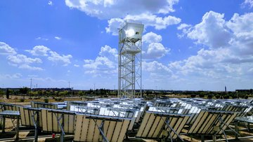 Gerüstartiger Turm inmitten von Photovolatikanlagen unter blauem Himmel