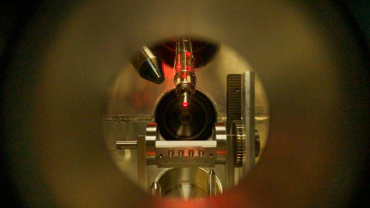 Blick in eine metallene Kammer: Ein Laserstrahl, mehrere Halterungen und Röhren sind sichtbar.