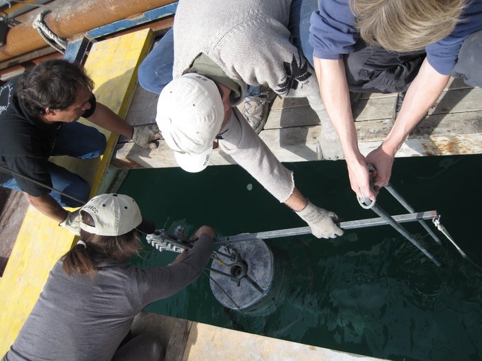 Sedimentprobe vom Genfer See Vier Forscher sitzen auf einer Plattform über dem See und ziehen einen Metallzylinder an die Oberfläche.