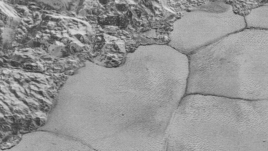 Aufnahme der Plutooberfläche: Die linke obere Bildhälfte zeigt eine Gebirgsregion, die rechte untere Bildhälfte eine Eisebene mit Dünenfeld.