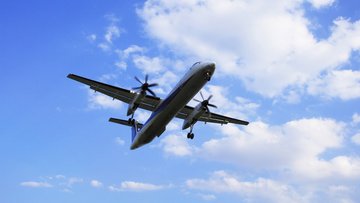 Ein großes Propellerflugzeug vom Boden aus gesehen, dahinter wolkiger Himmel