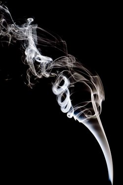 Rauch, der von einer Zigarette stammen könnte. Der Rauch wird beim Aufsteigen verwirbelt. Erst bilden sich symmetrische Wirbel, weiter oben werden die Formen des Rauchs chaotisch.