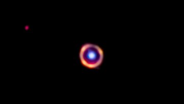 Leuchtende Ringstruktur auf dunklem Hintergrund. In der Mitte des Rings ist bläulich leuchtender Punkt im Vordergrund.