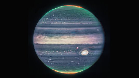 Der Planet Jupiter in blau-beigen Farbtönen. Die Polarlichter an den Polkappen sind grün und rot dargestellt. Der Hintergrund ist dunkel. 