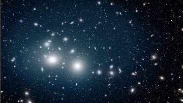 Viele Galaxien und Leuchtpunkte auf dunklem Hintergrund. Mittig links häufen sich Galaxien und zwei von ihnen leuchten besonders stark im Vordergrund.