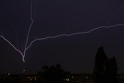 Nachthimmel mit Wolken wird durch einen starken Blitz erhellt, der in den Berliner Fernsehturm einschlägt.