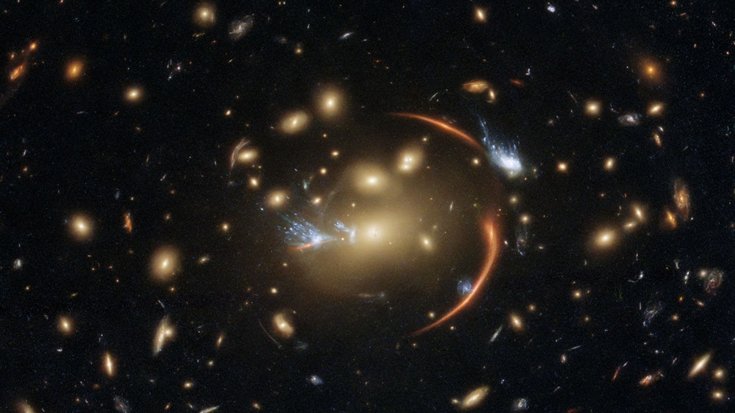 Ein Galaxienhaufen, darin zu langen Bögen gestreckte Bilder von Galaxien