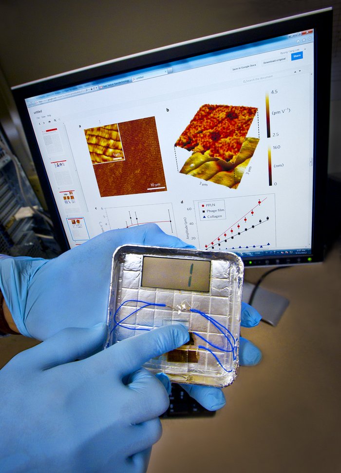 Elektrode mit Viren Zu sehen sind die Hände eines Forschers, eine Hand hält eine silberfarbene Schale mit der Elektrode, mehreren Kabeln und einem länglichen LCD-Bildschirm. Der Zeigefinger der anderen Hand drückt auf die Elektrode, auf dem LCD-Bildschirm erscheinen zwei blaue Striche. Im Hintergrund ist ein Computerbildschirm mit verschiedenen Mikroskopaufnahmen zu sehen.