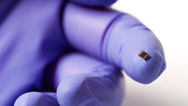 Eine winzige Vierfach-Solarzelle liegt auf einem behandschuhten Zeigefinger.