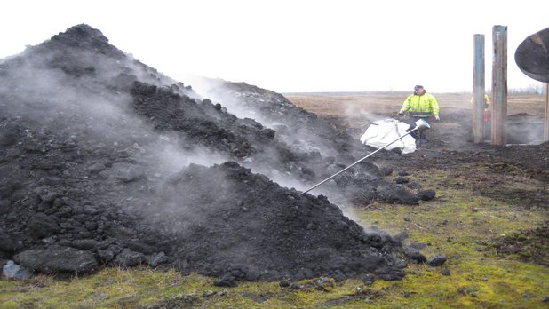 Ein Mensch steht hinter einer schwelenden Kohlehalde.